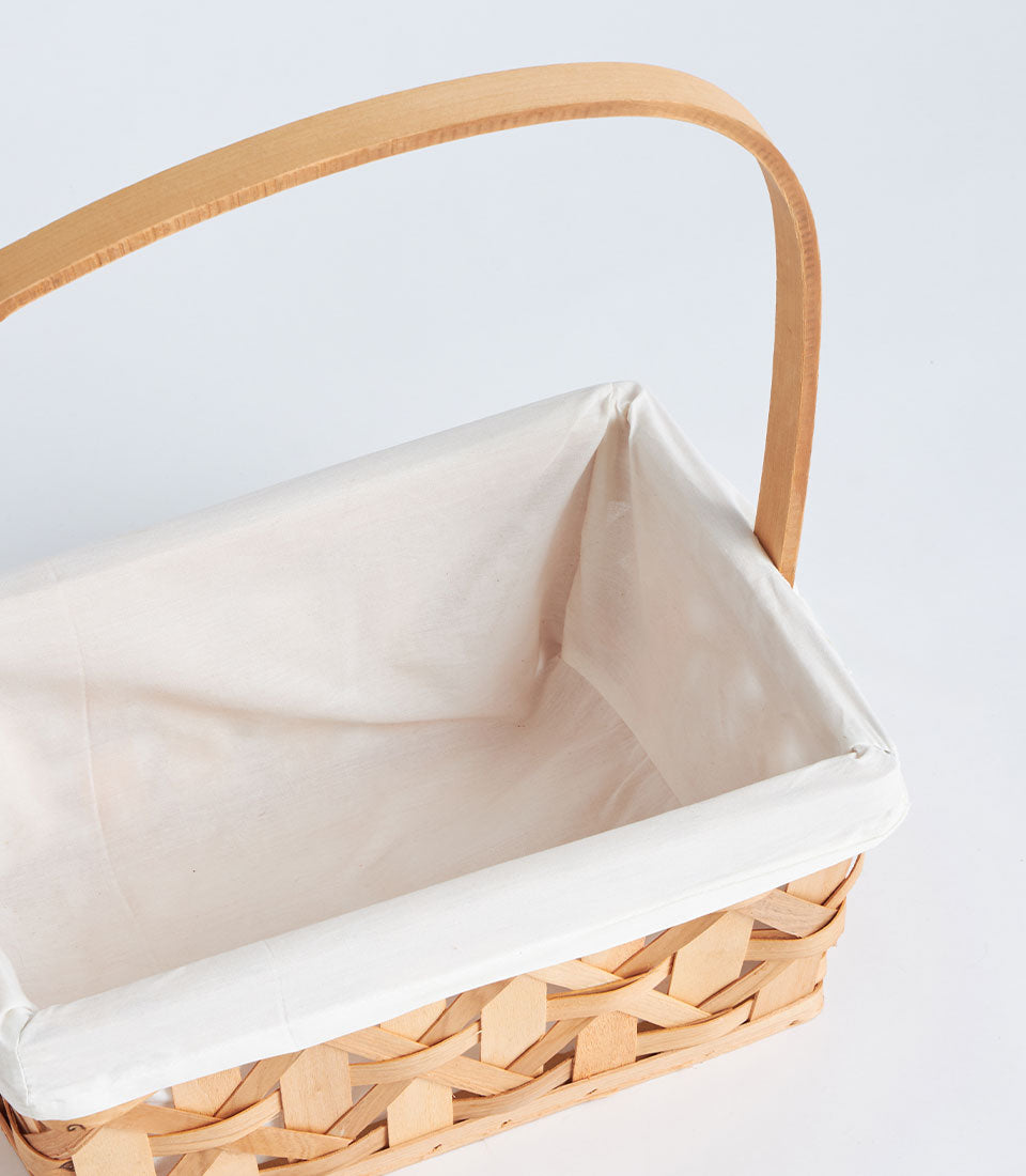 Handwoven rectangular wicker basket with tall wooden handle and cream fabric lining