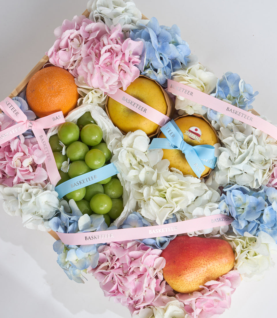 # Alt Text

Luxury fruit and flower gift basket with pink peonies, blue hydrangeas, white flowers, oranges, lemons, green apples, and pink/blue ribbons labeled "Basketeer."