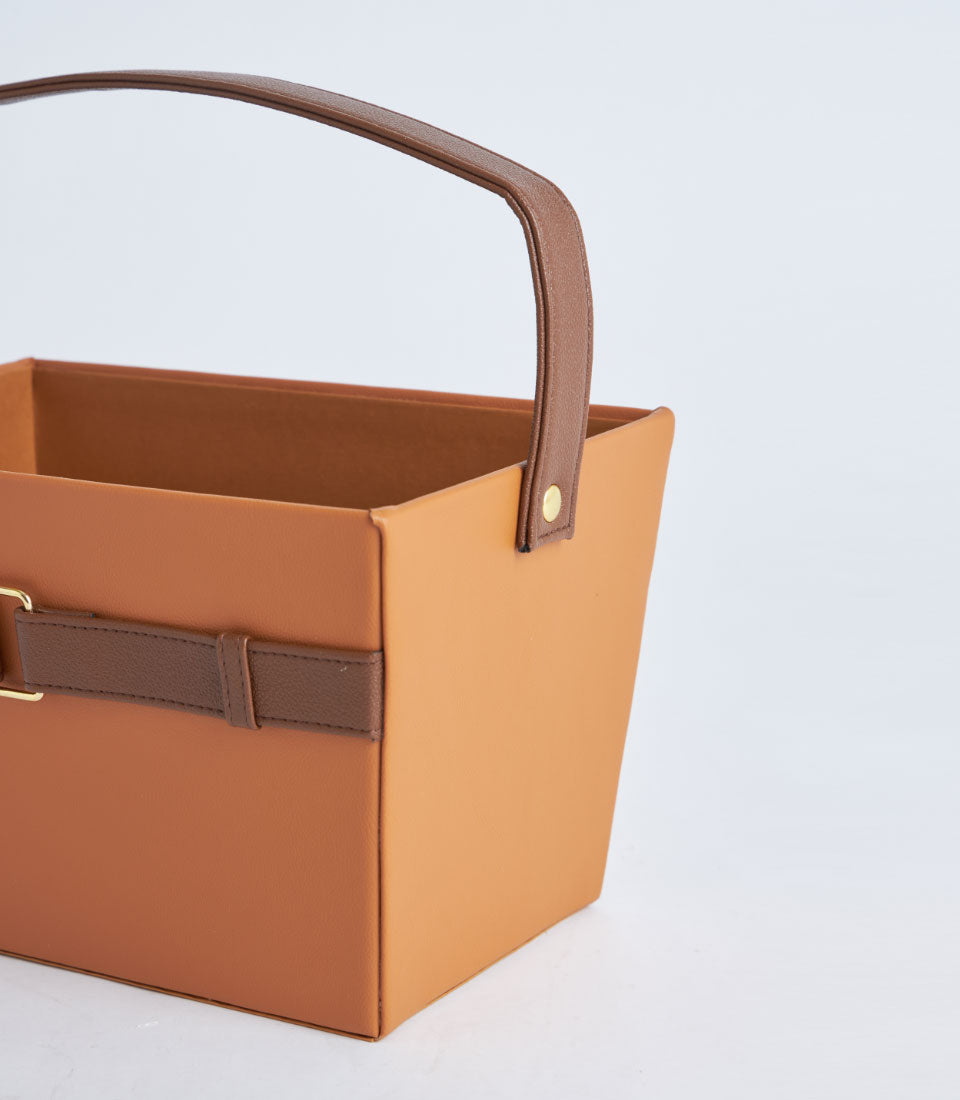 Tan leather gift basket with dark brown handle strap and gold buckle hardware