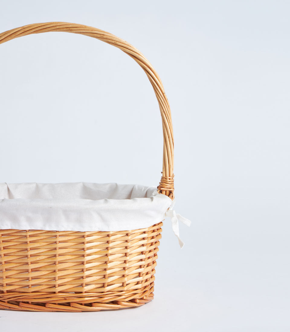 Light brown wicker oval basket with arched handle and white fabric lining