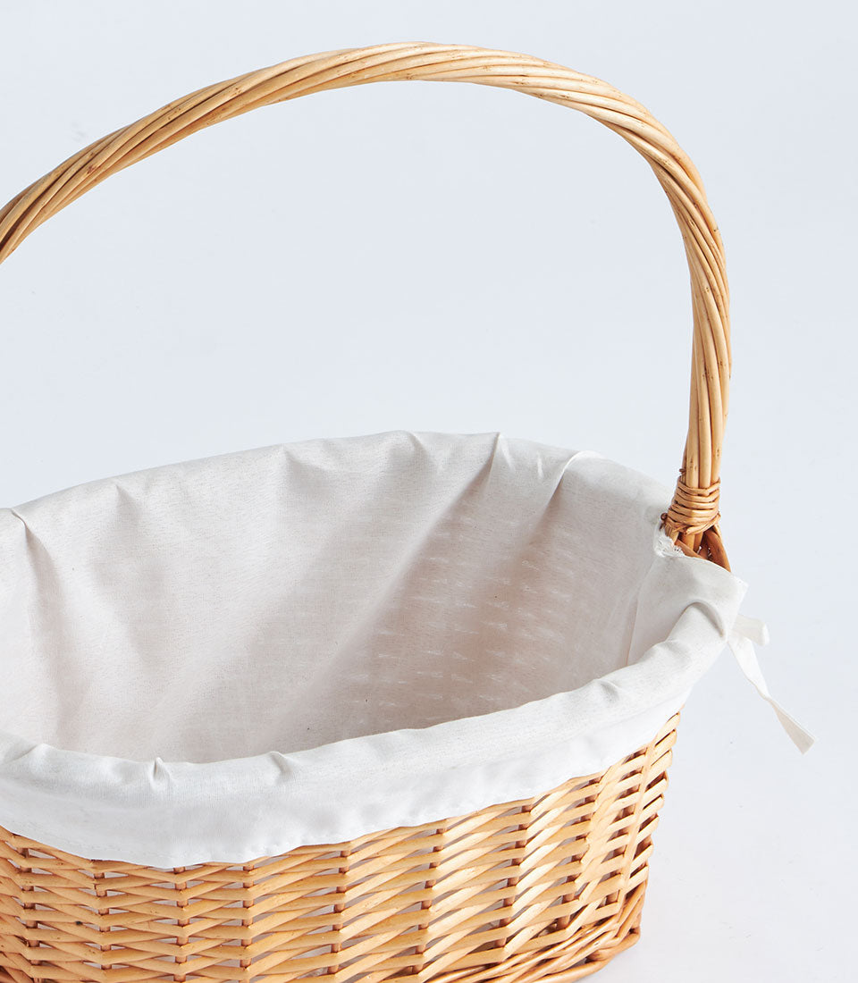 Light brown wicker oval basket with arched handle and white fabric lining