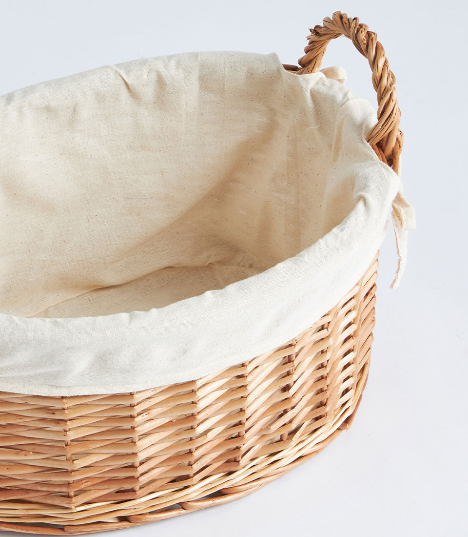 Natural wicker oval gift basket with cream fabric lining and braided handles