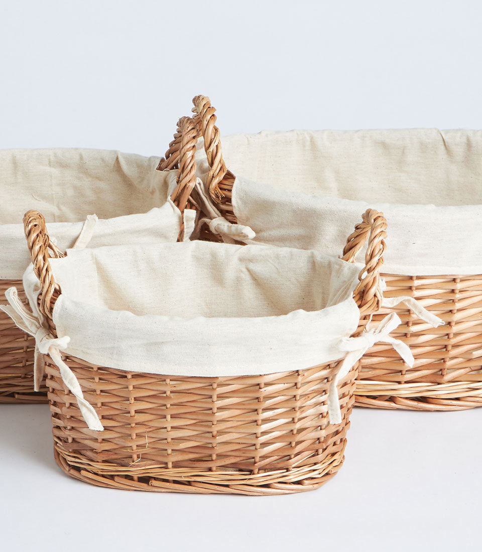 Set of three handwoven oval wicker baskets with beige fabric linings and braided handles