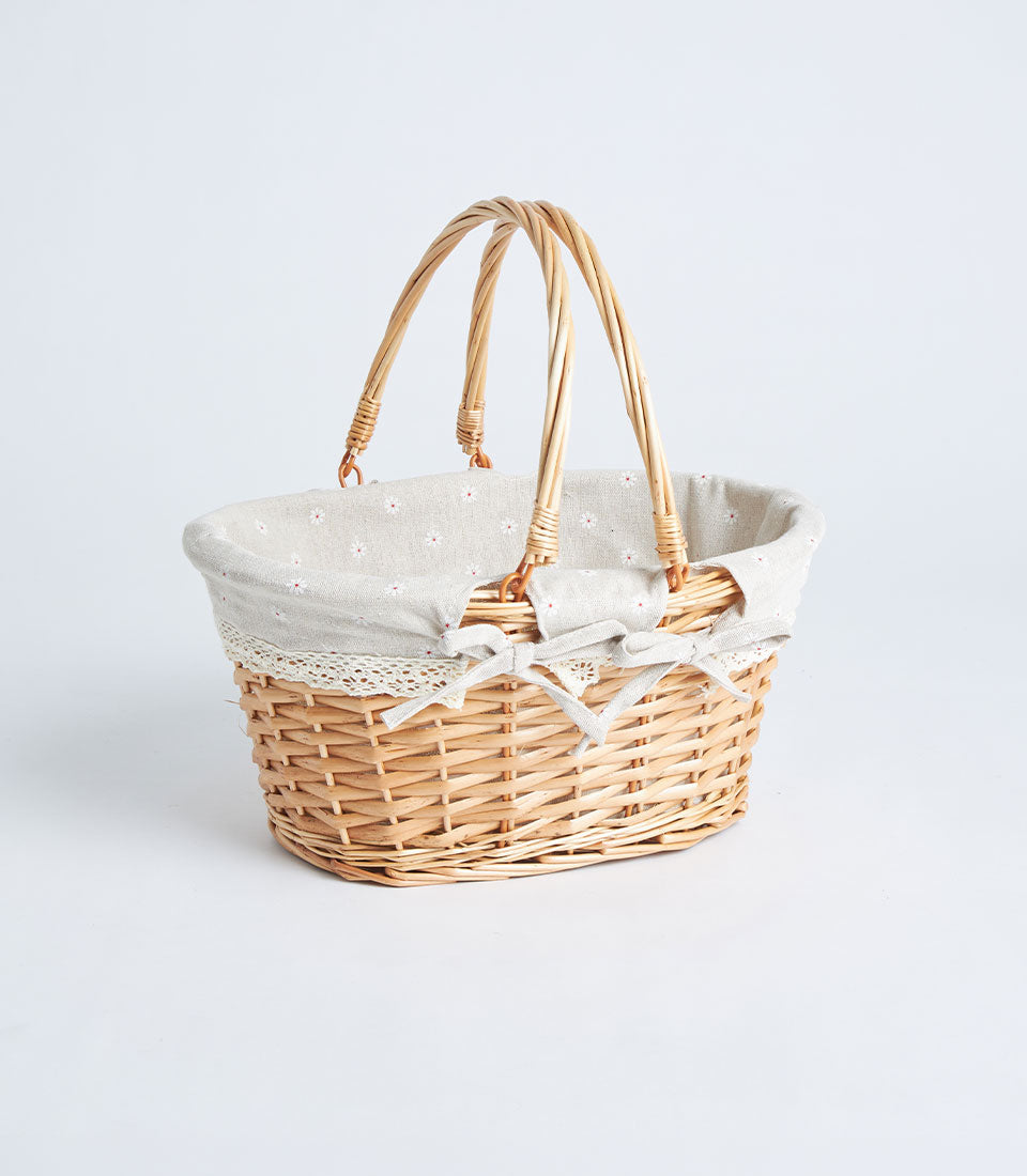 Handwoven oval wicker basket with double handles, light beige floral fabric lining, and lace trim