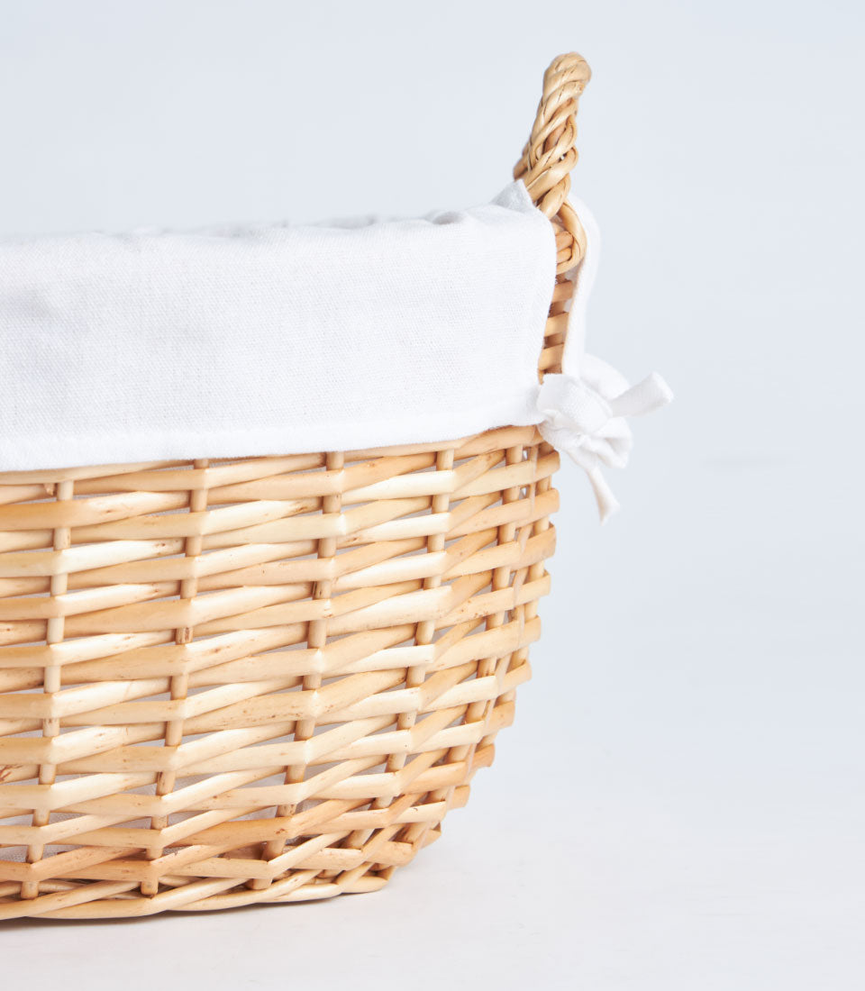 Large natural wicker oval basket with cream linen lining and handles, ideal for luxury gift presentations