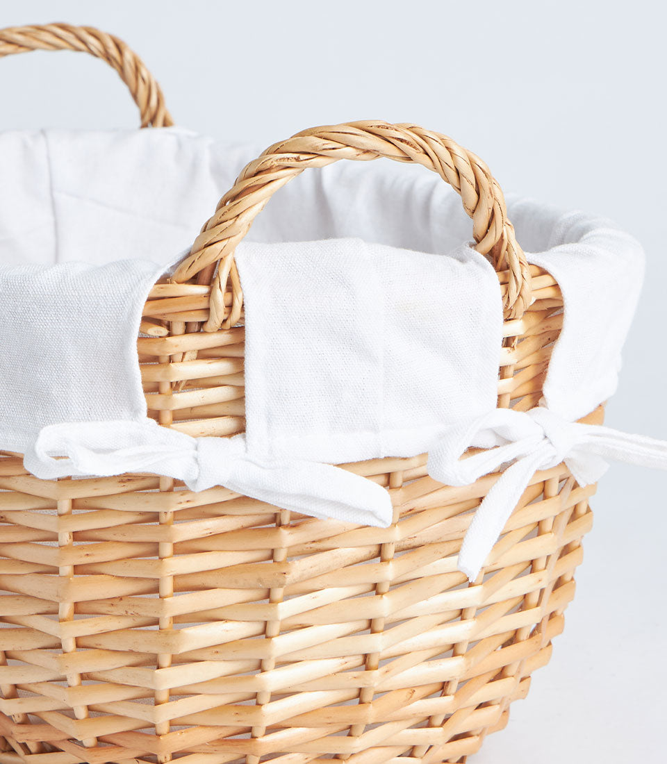 Natural wicker oval gift basket with white linen lining and handles