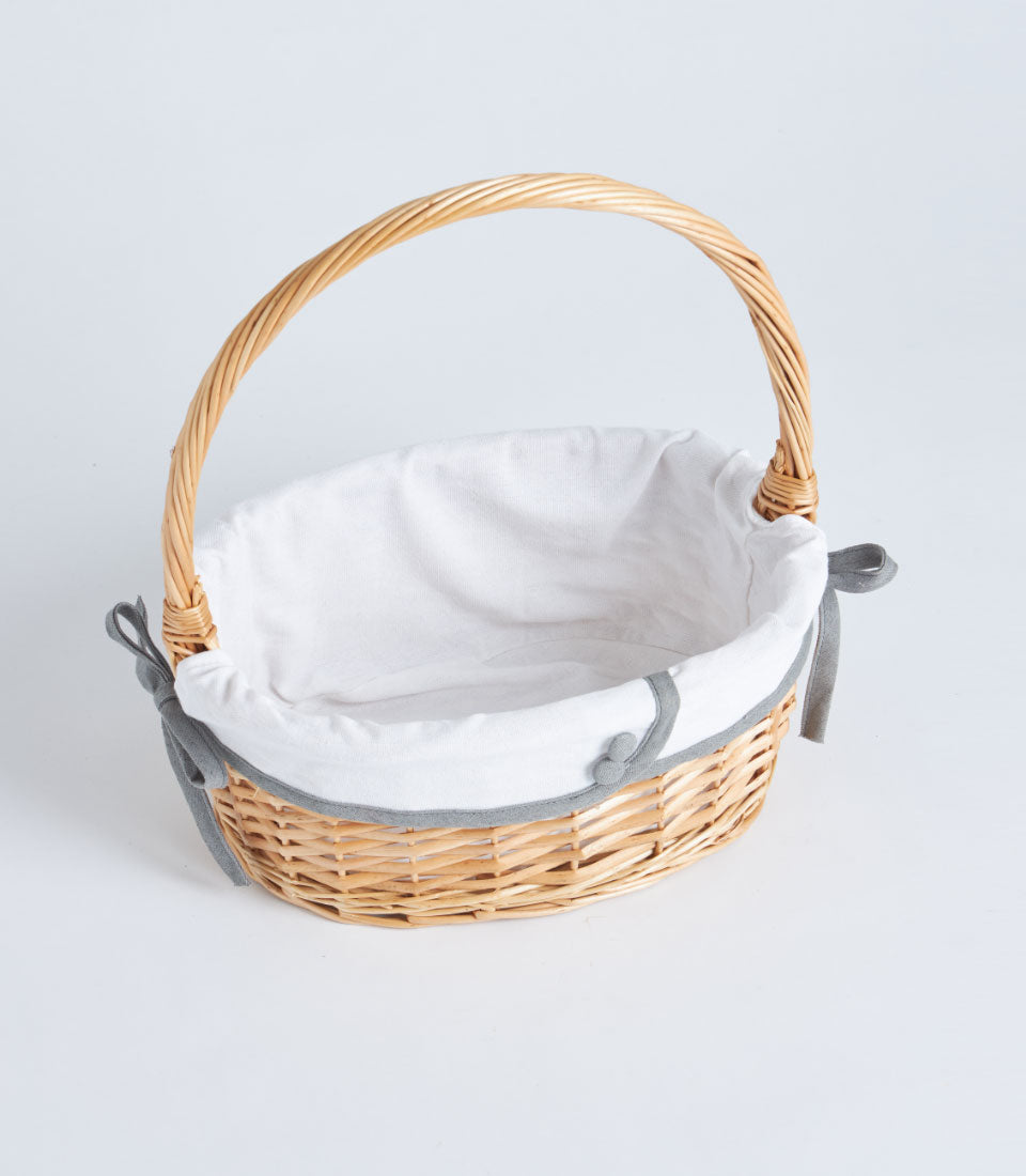 Handwoven oval wicker basket with arched handle and white fabric lining, ready for custom gift filling