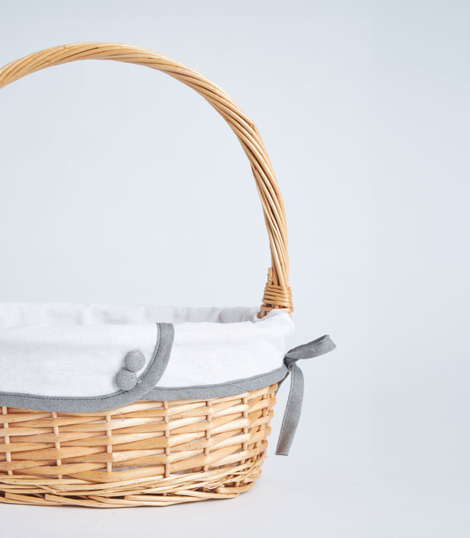 Light brown handwoven wicker basket with white fabric liner and grey ribbon bow