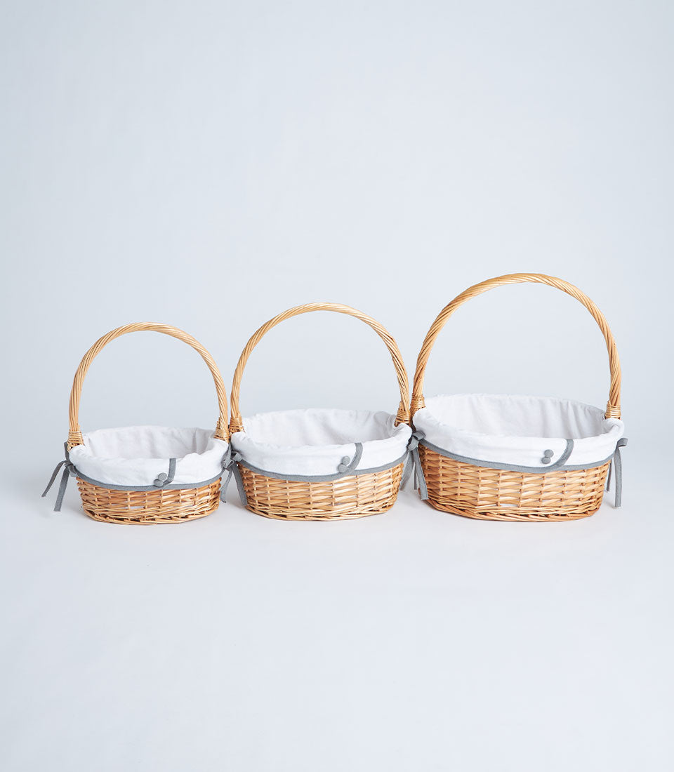 Graduated set of three handwoven light brown wicker baskets with single handles and white fabric liners with grey trim