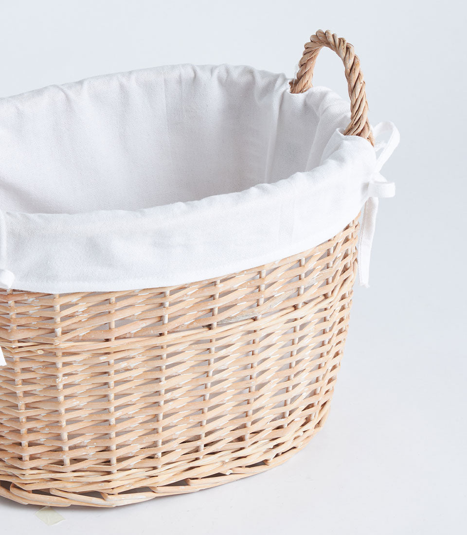 Light wicker oval basket with white fabric lining and braided side handles, artisan handwoven storage for home or gifting