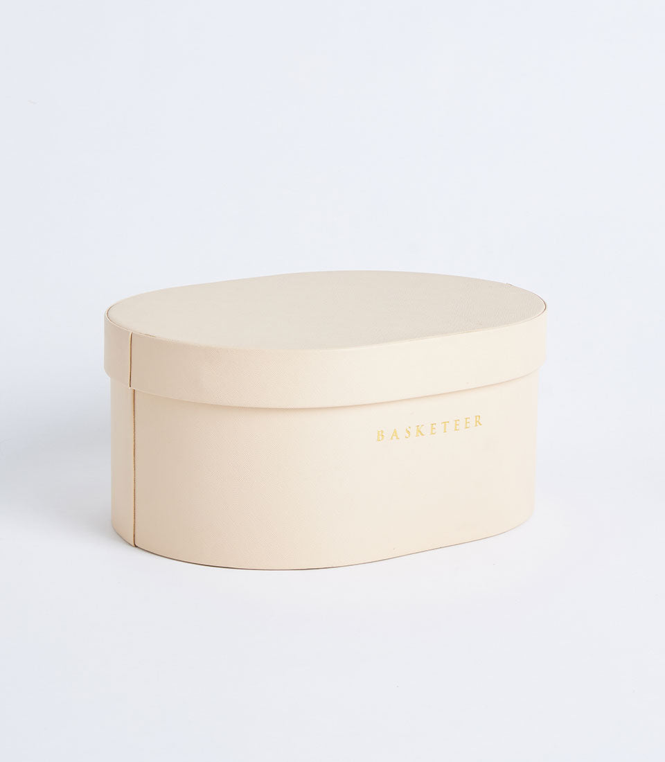 Beige round leather storage box with metallic gold Basketeer branding and removable lid