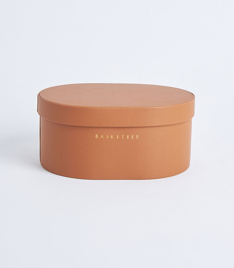Round tan leather storage box with gold embossed Basketeer branding