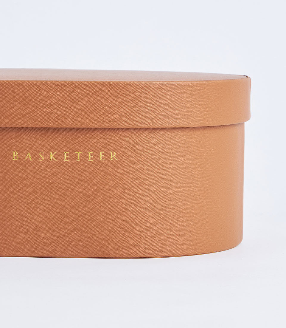 Warm terracotta round leather storage box with gold embossed Basketeer branding and removable lid