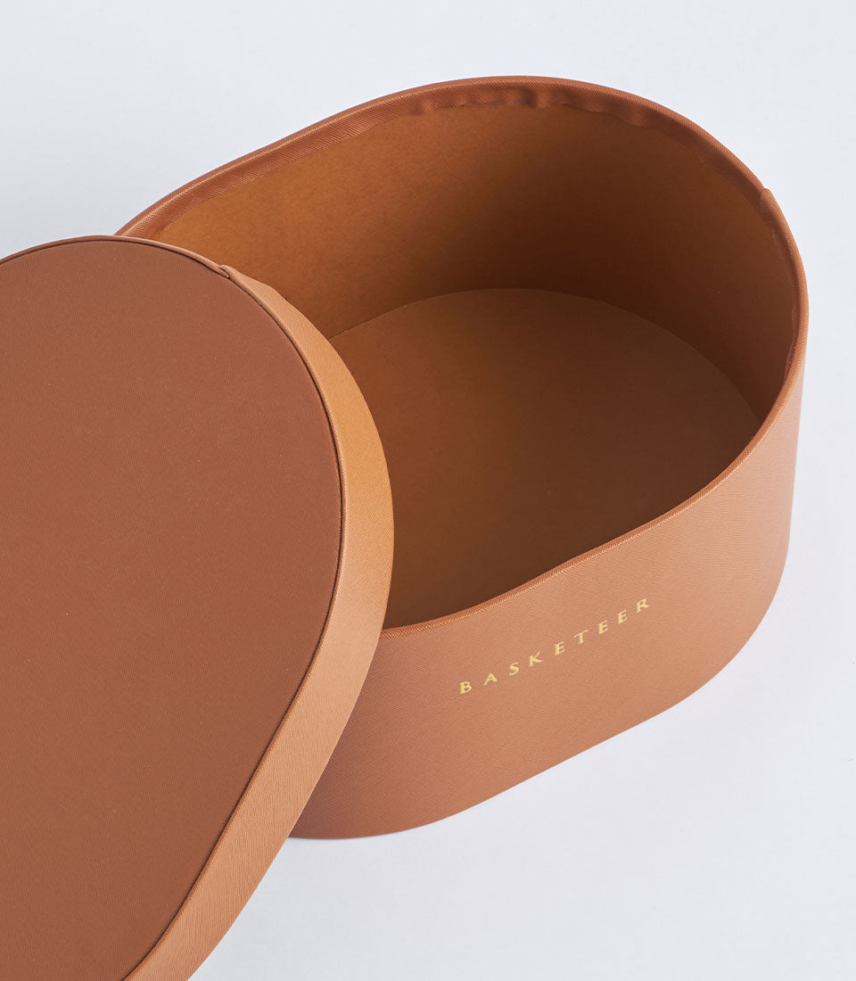 Round leather storage box with gold debossed Basketeer branding, open lid revealing smooth brown interior