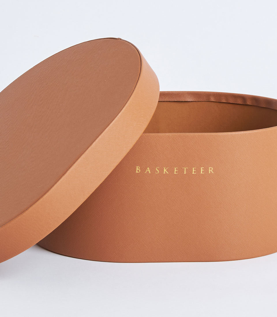 Round matte tan leather storage box with gold Basketeer branding and satin-lined interior