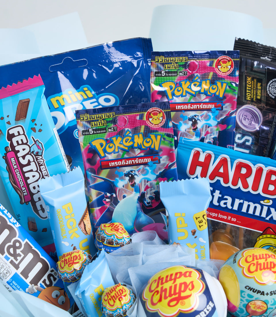 Colorful gift collection featuring Pokemon trading card booster packs, Chupa Chups lollipops, Haribo candy, and mini Oreo boxes arranged on light blue tissue paper.