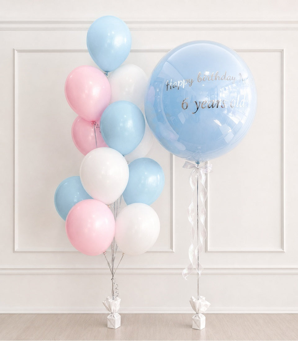 Blue and pink balloon bouquet with white accents, featuring a large bubble balloon with "Happy birthday 6 years old" text and ribbon ties.