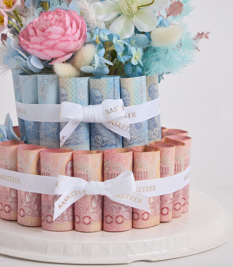 # Alt Text

Tiered money cake with rolled banknotes in blue and pink, white ribbons, fresh flowers including pink peonies and blue hydrangeas on top.