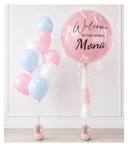 Pink and blue balloon arrangement with large personalized "Welcome to the World Mona" sphere balloon and tassel decorations.