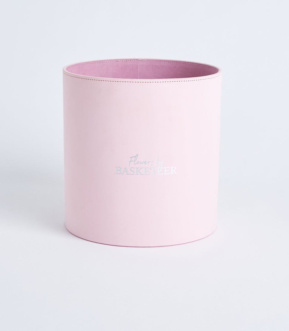 Blush pink cylindrical flower gift box with metallic Basketeer branding and fabric-lined interior