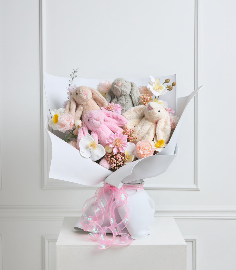 Luxe floral bouquet with cream bunny plushies, pink and white flowers, wrapped in white paper with pink ribbon bow.
