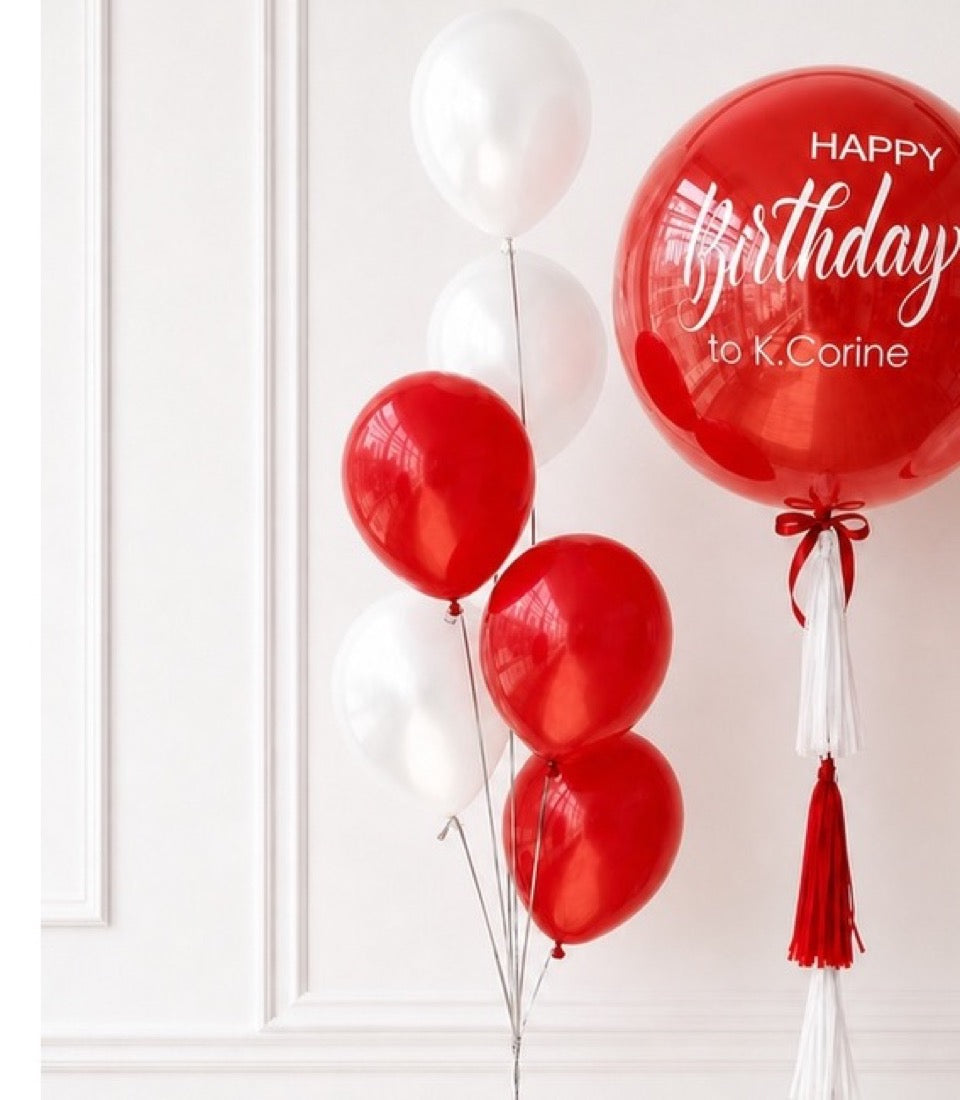 Red and white helium balloons with "Happy Birthday to K.Corine" text on large red balloon, decorated with red and white tassels.