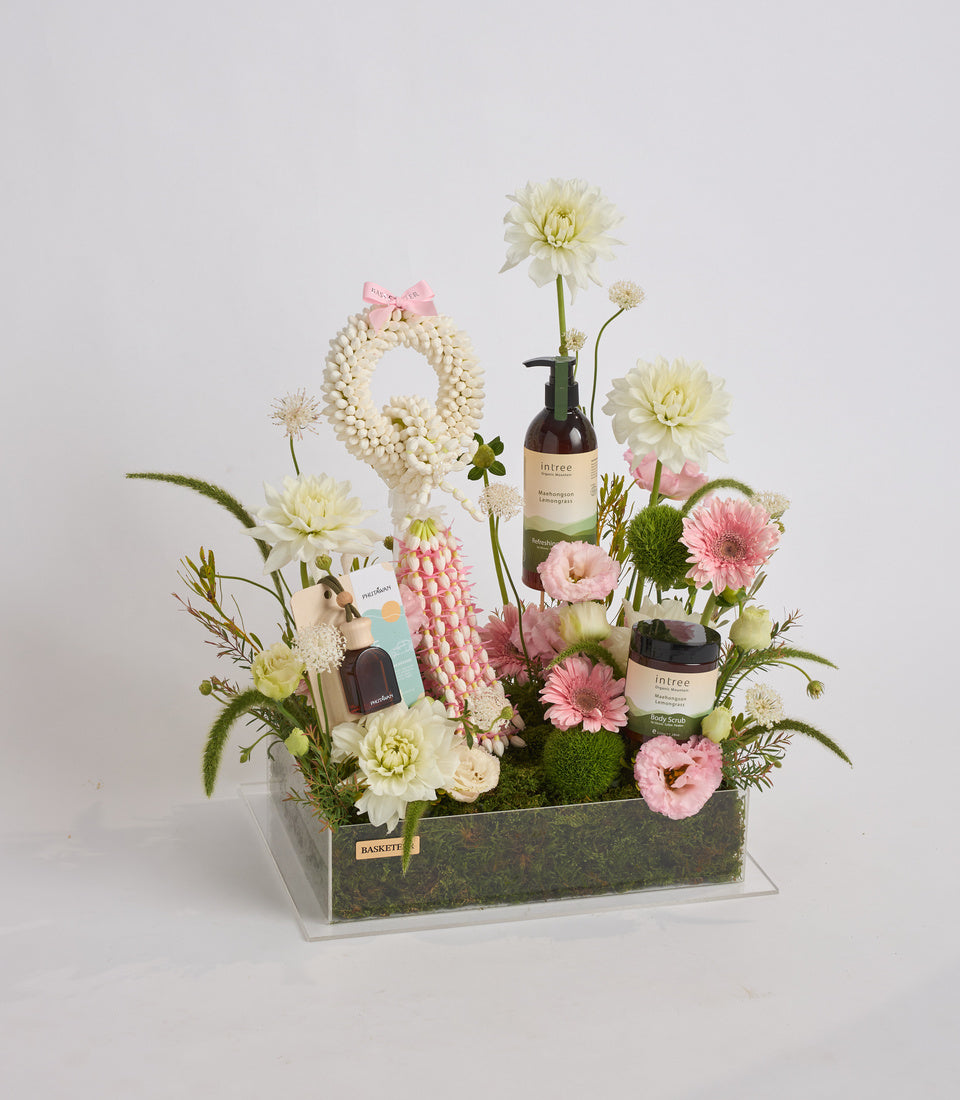 Luxury floral gift arrangement with cream and pink dahlias, gerberas, white flowers, intree skincare products, beaded wreath, moss base in rectangular container.