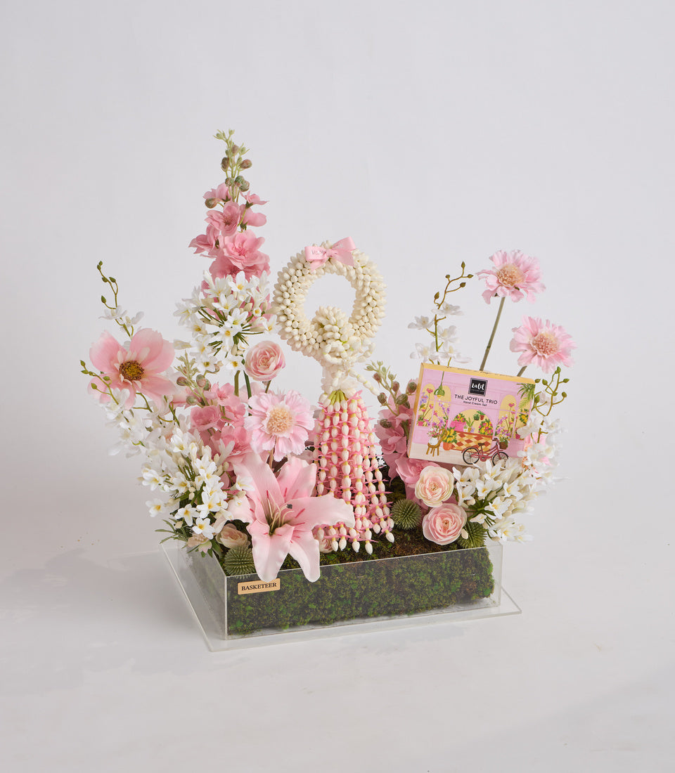 Luxury floral arrangement in clear box with pink and white flowers, pearl beaded wreaths, coral beads, moss base, and decorative book accent.