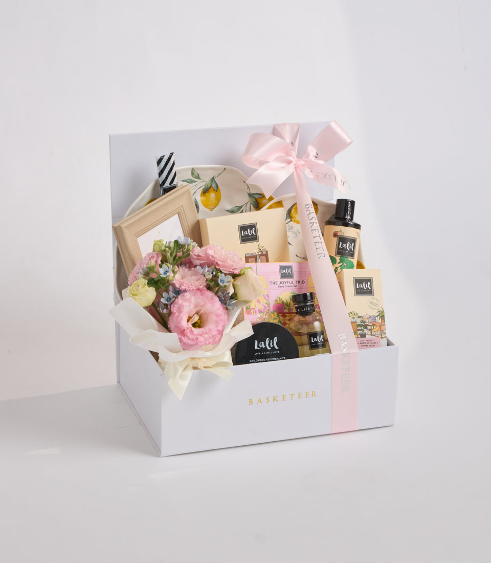 # Alt Text

Luxe gift basket with pink flowers, beauty products, wooden frame, and pink ribbon bow in white box labeled Basketeer.