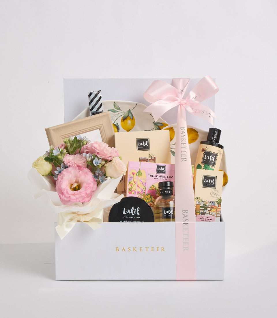 Luxury gift basket featuring pink flowers, Lalif beauty products, lemon-patterned box, wooden frame, and pink ribbon bow on white Basketeer box.