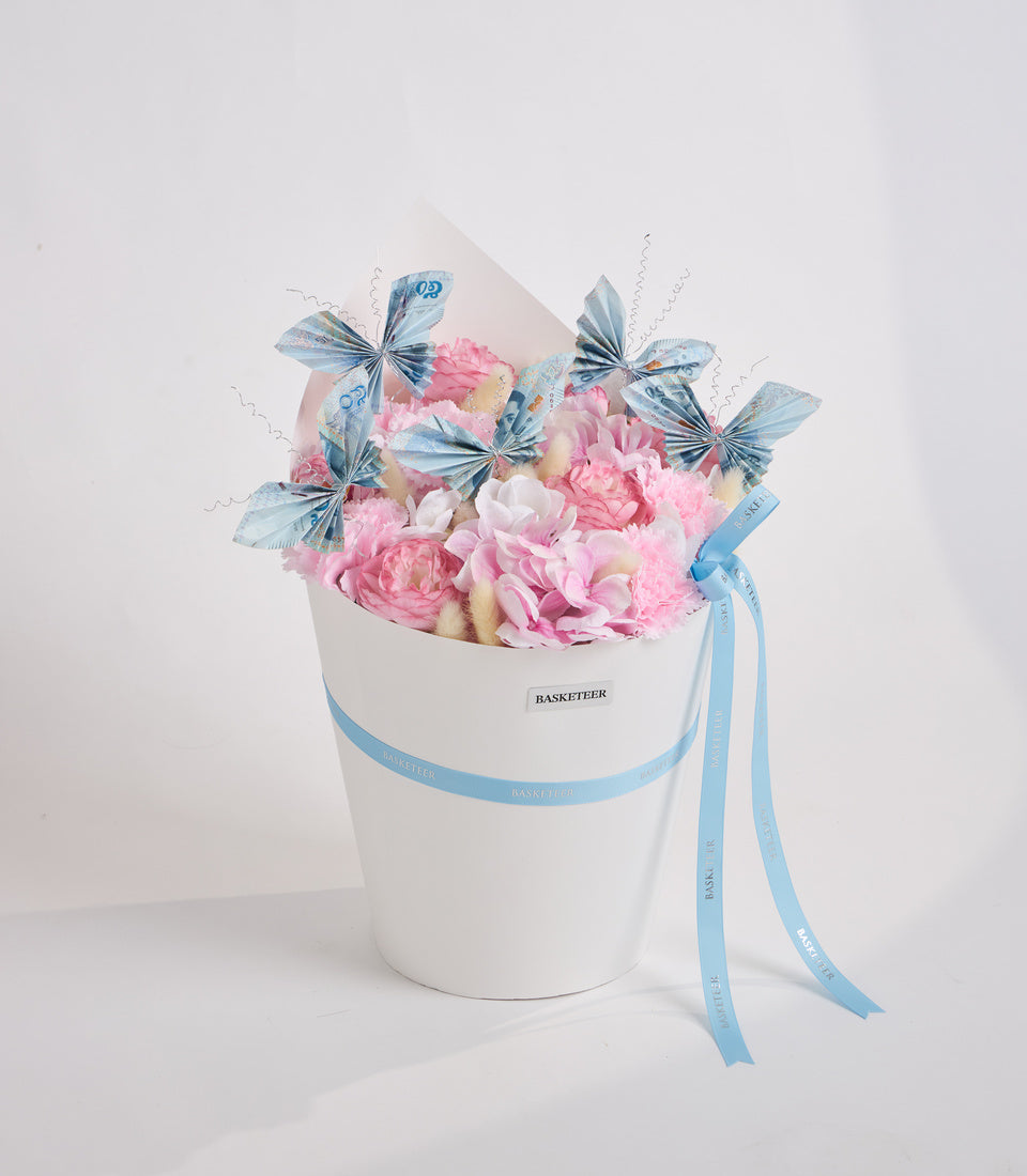 Luxurious white cylindrical hat box filled with pink peonies and white flowers, decorated with blue patterned butterflies and blue ribbons, branded "BASKETEER".