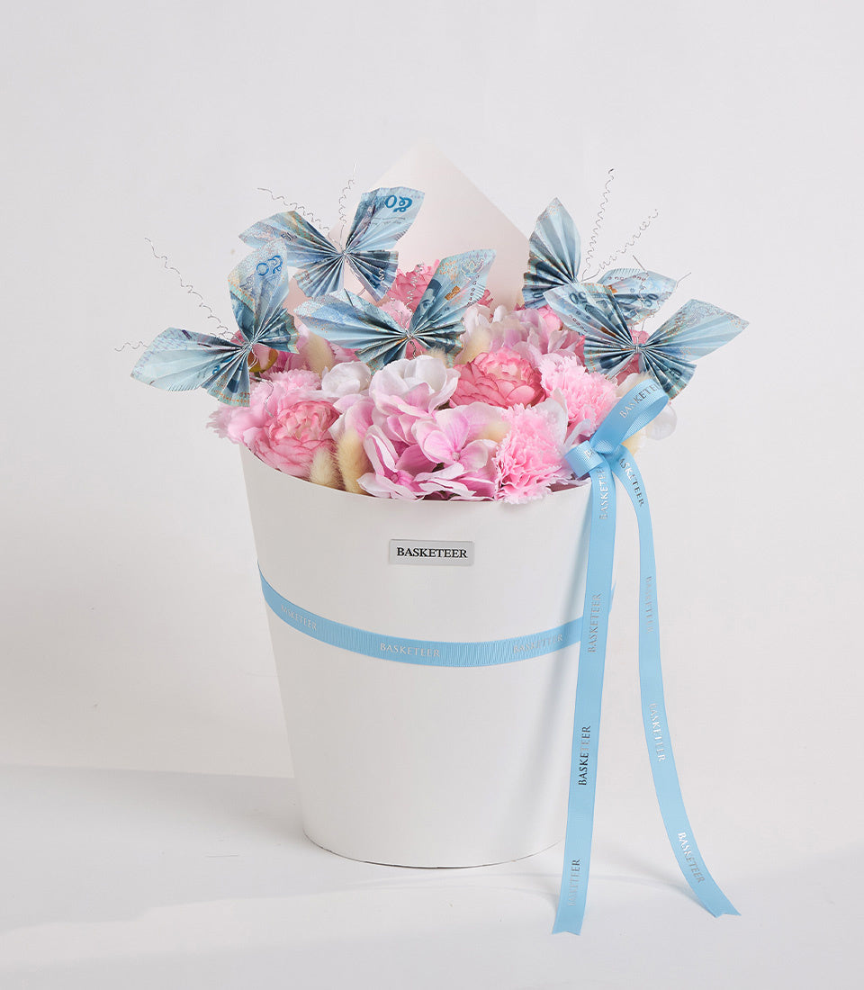 White cylindrical flower box with pink peonies, white flowers, blue decorative butterflies with antennae, and blue ribbon bow by Basketeer.