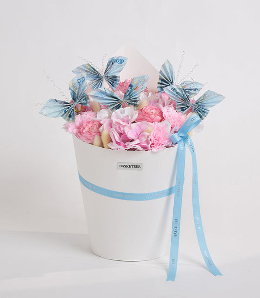 White cylindrical flower box with pink peonies, white flowers, blue decorative butterflies with antennae, and blue ribbon bow by Basketeer.