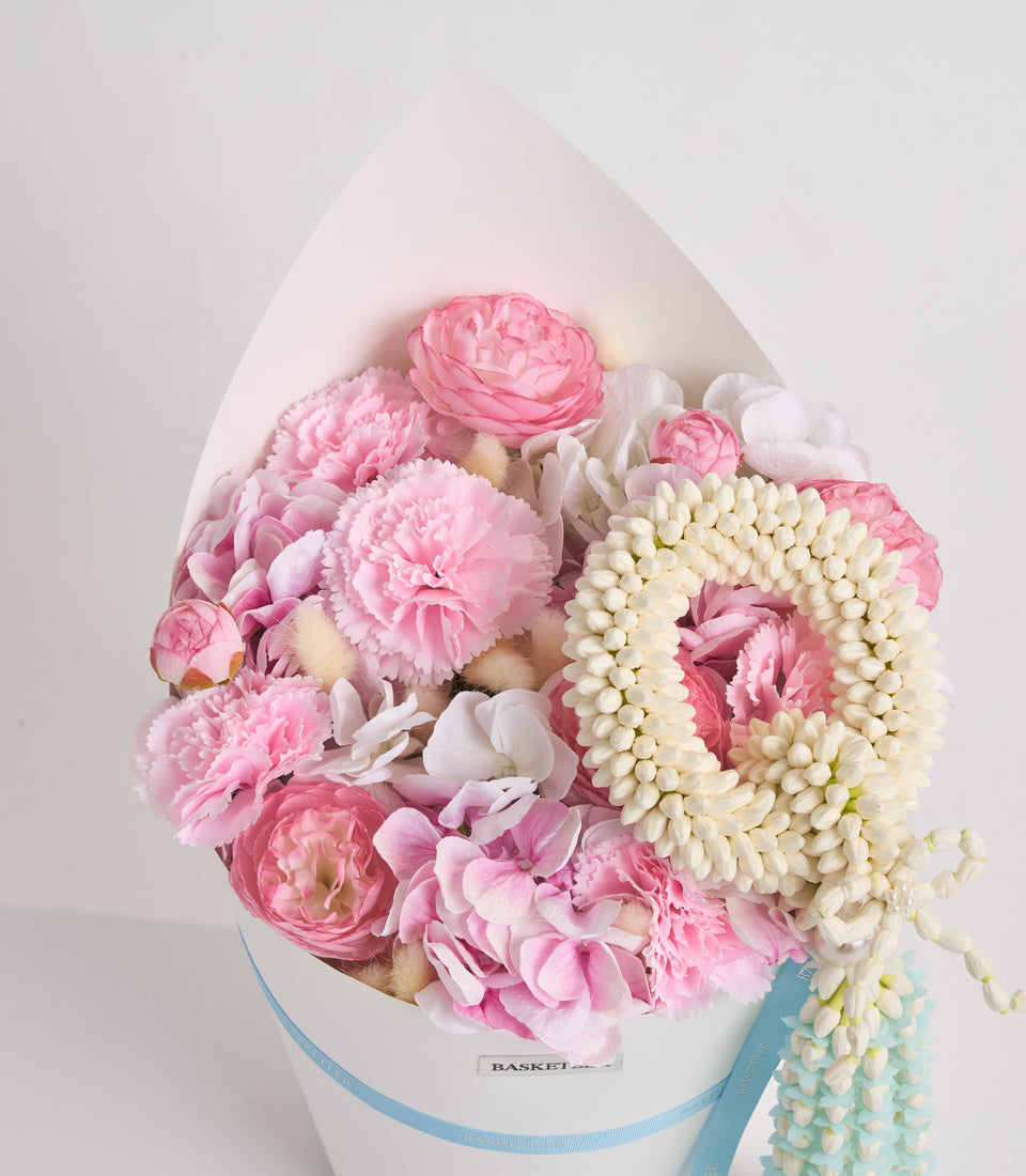 Luxurious floral arrangement in white egg-shaped box with pink peonies, roses, white hydrangeas, and cream flower beads, tied with blue ribbon.