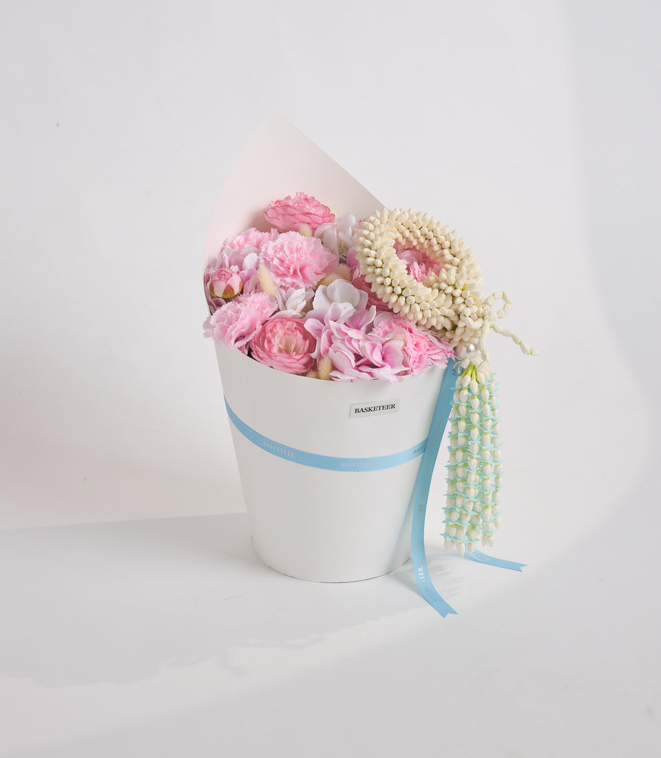 Luxurious white cylindrical flower box with blue ribbon band, featuring pink peonies, cream spray roses, and pale green hanging amaranthus with draped ribbon.