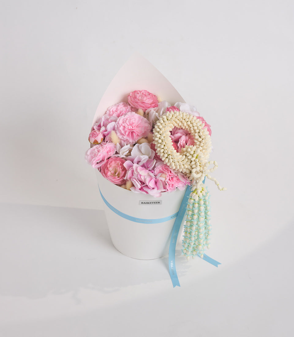 Luxurious floral arrangement in white hat box with pink roses, cream jasmine garland, and blue ribbon accent on white background.