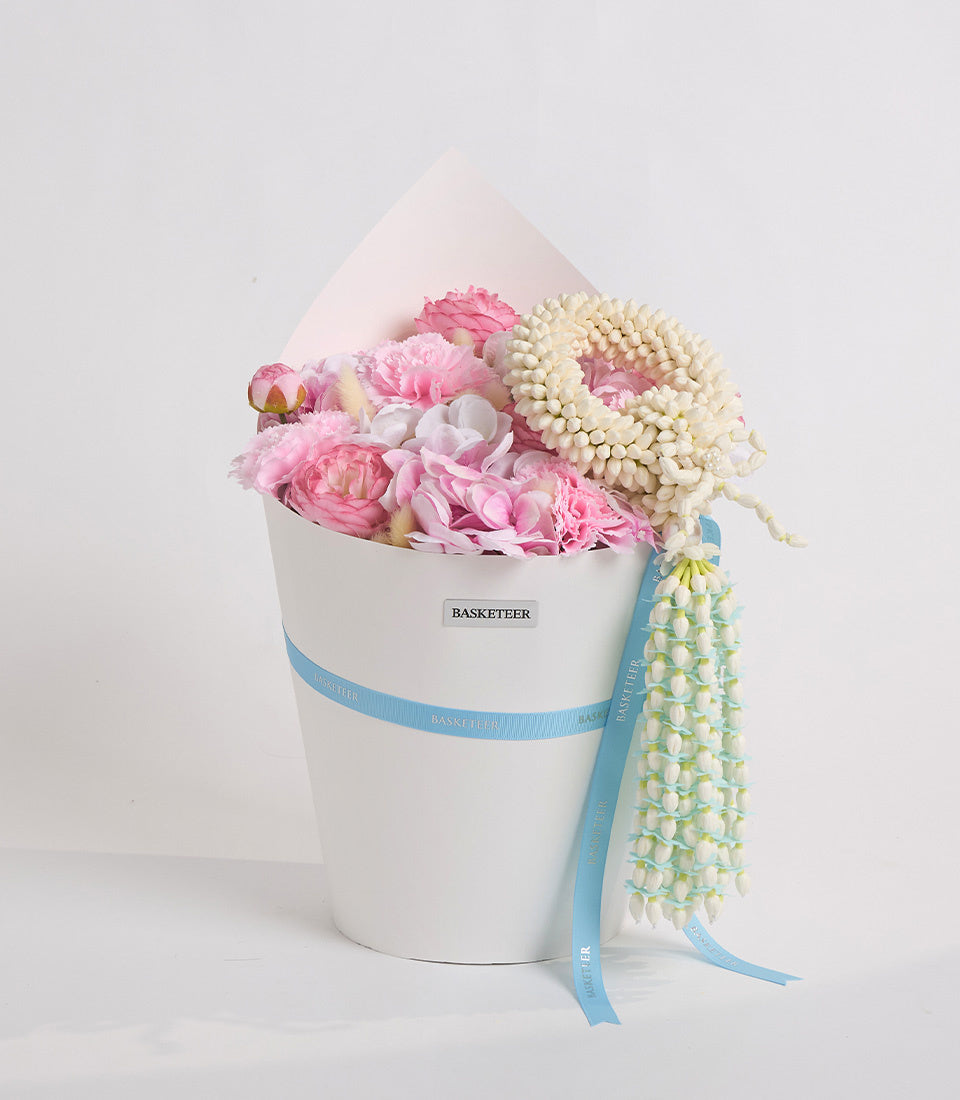 Elegant white cylindrical box with blue ribbon containing pink peonies, cream spray flowers, and beaded pearl garland strands.