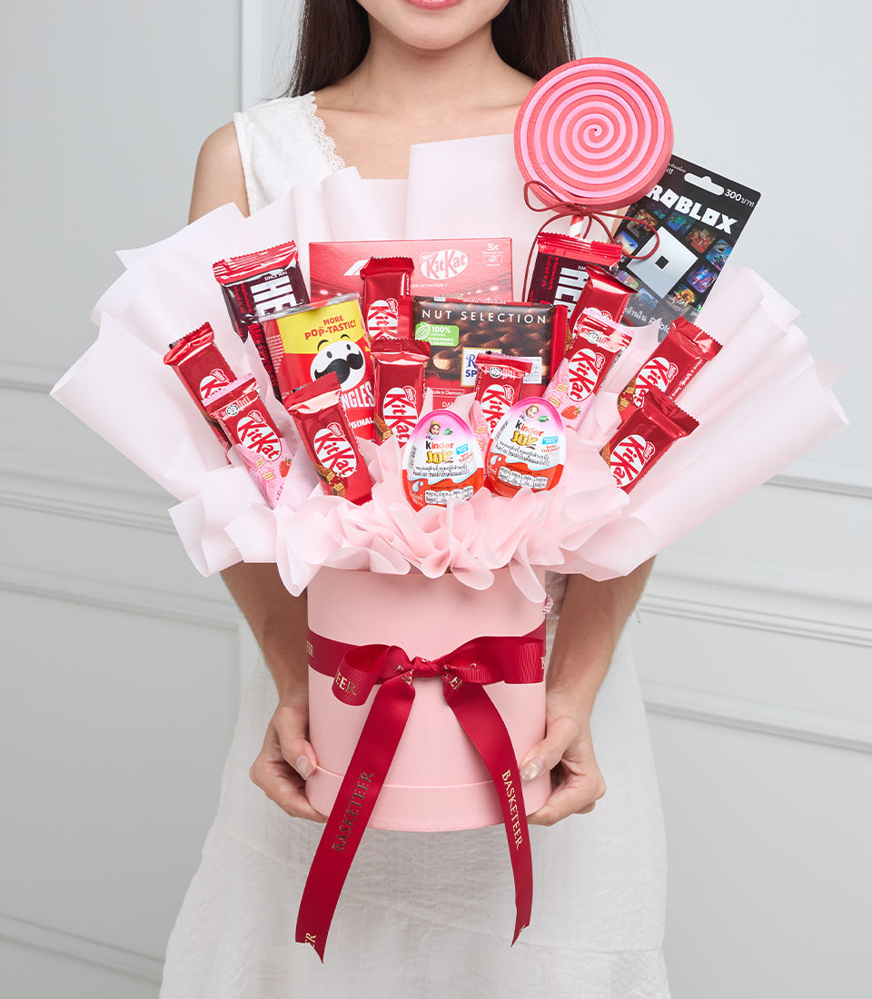 # Alt Text

Woman holding a pink candy bouquet arrangement with red and white snack items, KitKat products, lollipop, and red ribbon bow.