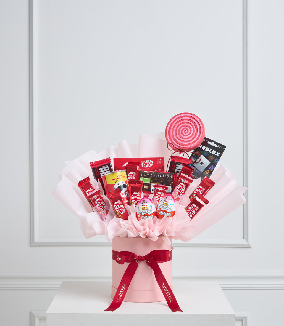 Red and pink gift bouquet featuring KitKat chocolates, sweets, and a spiral lollipop, arranged in pink tissue paper with red ribbon bow.