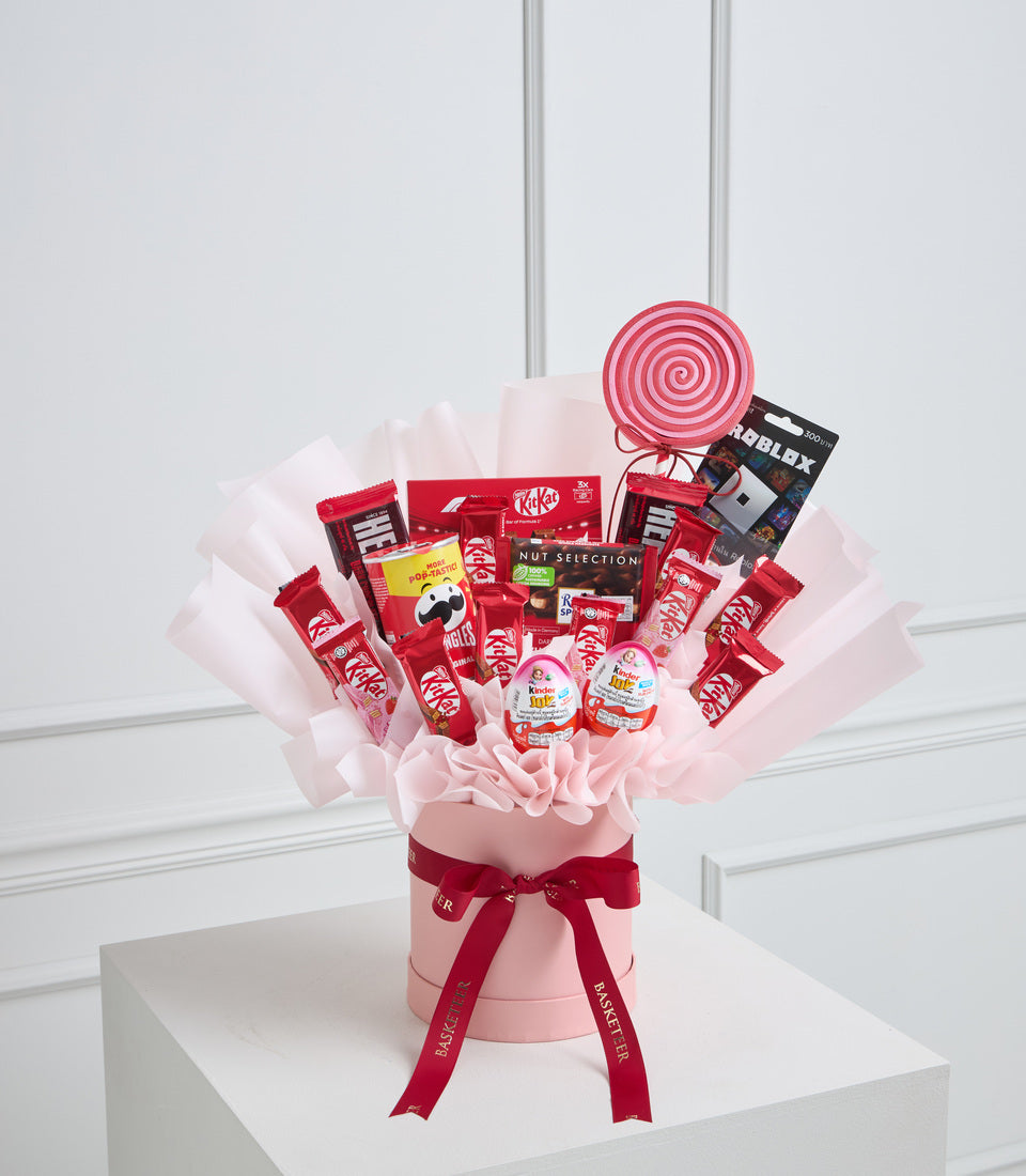 Red and pink candy bouquet with Kit Kat, lollipop, and assorted sweets in pink tissue-wrapped vase with red ribbon bow.