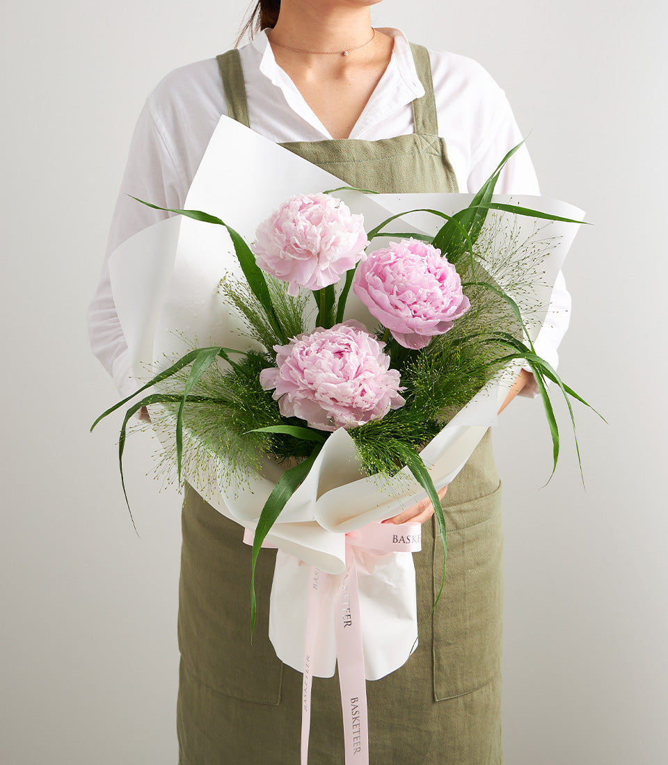 Three vibrant pink peony blooms nestled amongst lush green foliage, elegantly wrapped in crisp