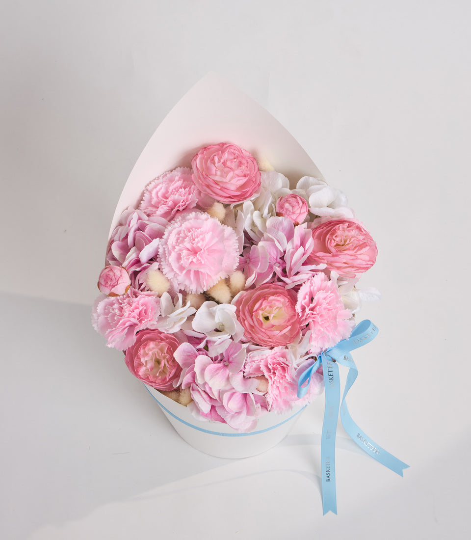 Luxury floral arrangement in white egg-shaped box with pink peonies, roses, white flowers and blue ribbon bow.