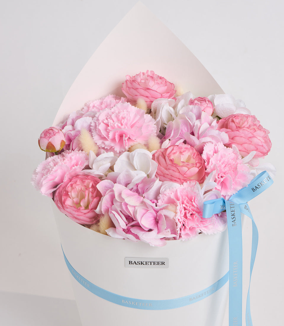 Luxury pink and white peony flower arrangement in white hatbox with blue Basketeer ribbon bow, elegant gift presentation.