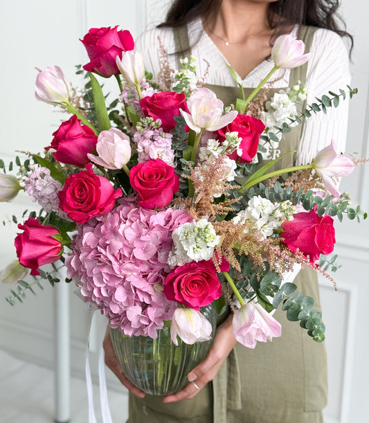 A luxurious vase arrangement from Flowers by Basketeer featuring vibrant fuchsia roses,