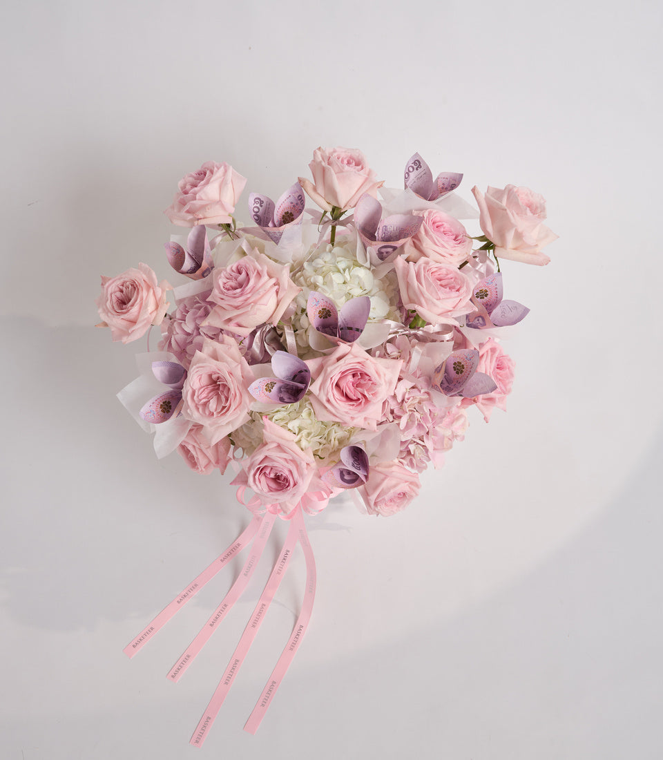 Heart-shaped bouquet of pink roses and white hydrangeas with purple orchids, tied with pink ribbons on white background.