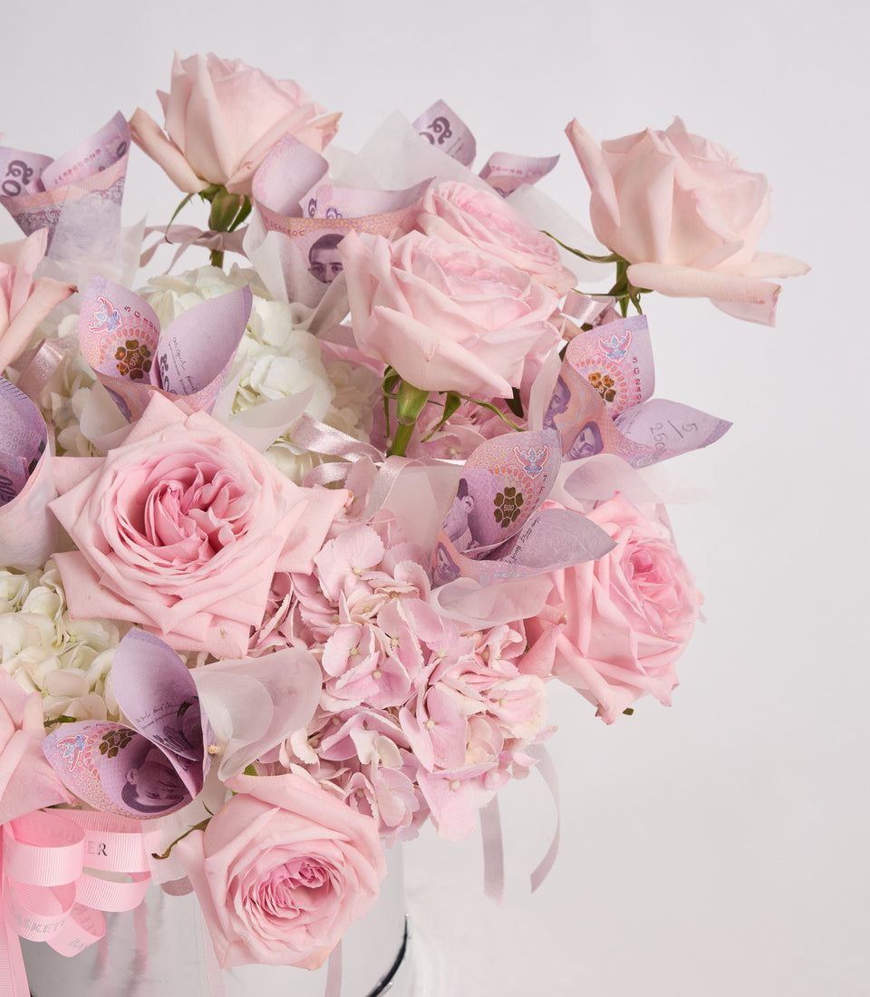 Luxurious bouquet of pink roses and hydrangeas with decorative purple banknote ribbons and bows in white vase.