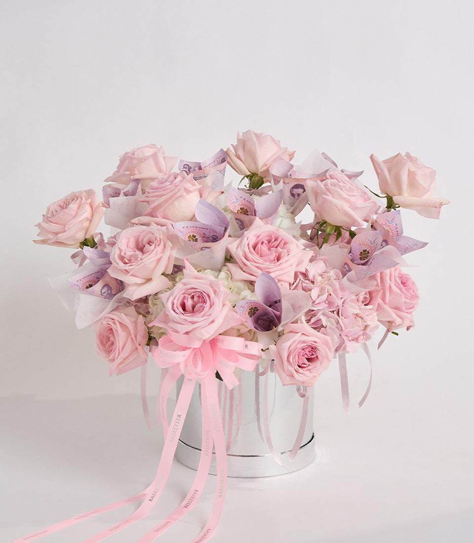 Luxurious pink rose bouquet with purple orchids and white hydrangeas in a white ceramic vase, tied with pink ribbon.