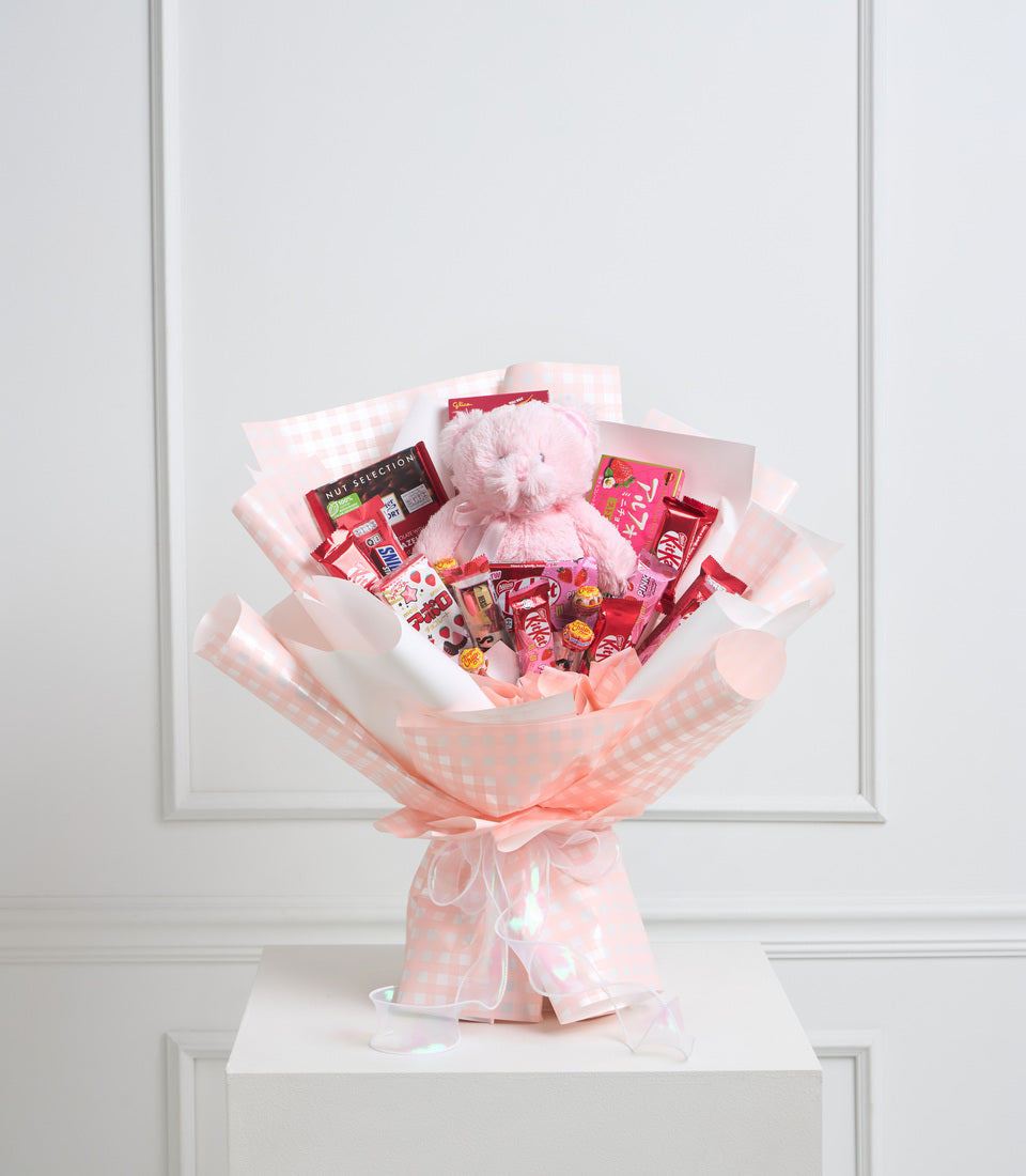 # Alt Text:

Pink and white checkered gift bouquet with plush teddy bear, assorted red candies, chocolates, and sweets wrapped in cellophane on white pedestal.