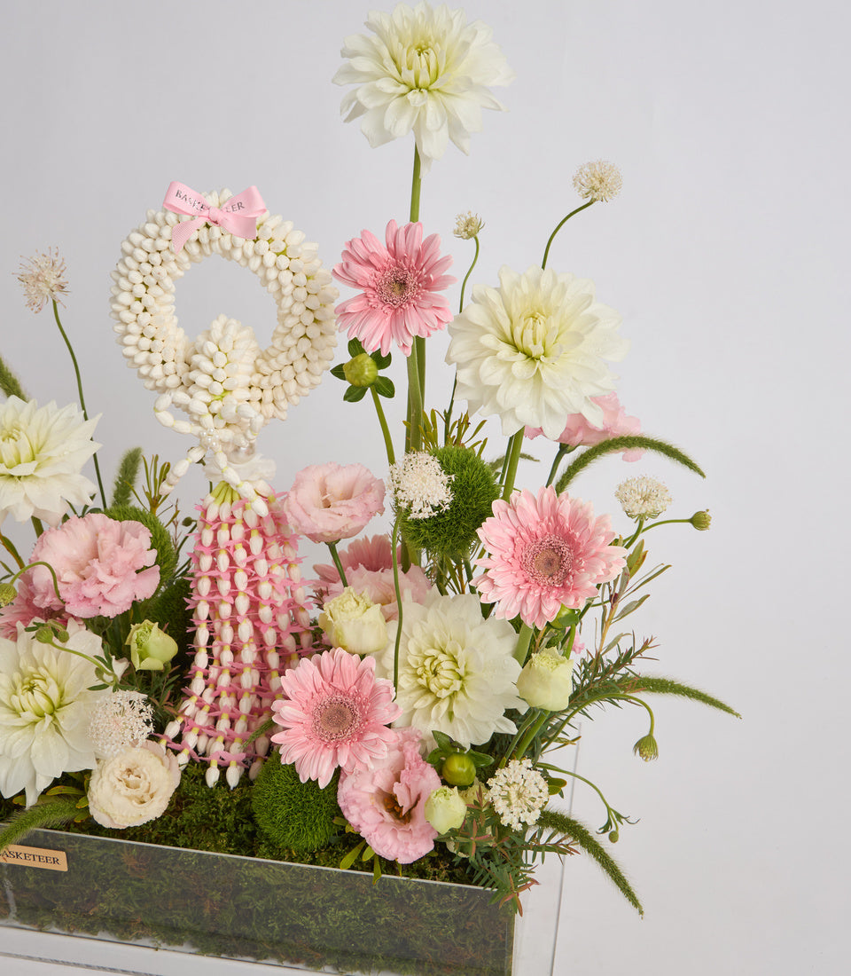 Elegant floral arrangement in rectangular container with white dahlias, pink gerberas, white pearl strand detail, and green moss base against neutral background.