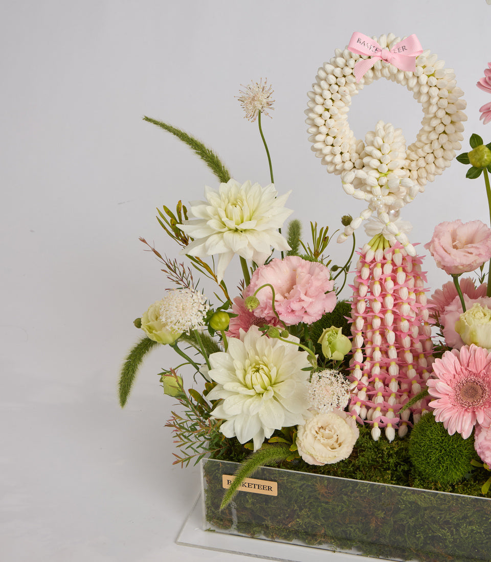 # Alt Text

Elegant floral arrangement in rectangular vase featuring white dahlias, pink gerberas, cream roses, pearl bead garland, and decorative pink bow on gray background.